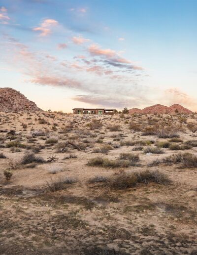 Desert landscape at dusk with abandoned structures and sparsely vegetated terrain.