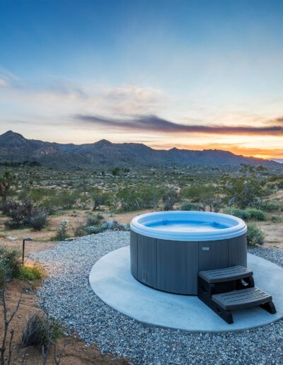 A hot tub with steps placed on gravel, overlooking a scenic desert landscape at sunset.