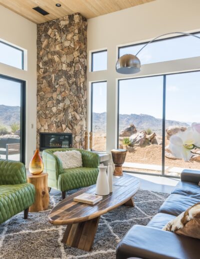 Modern living room with large windows, a stone fireplace, and desert views.