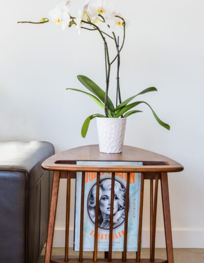 A vase with white orchids on a wooden side table with magazines on the shelf below.