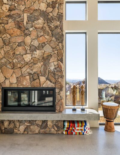 Modern interior with stone wall, fireplace, and floor-to-ceiling windows offering mountain views.