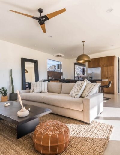 Modern living room with beige sofa, wooden coffee table, and a ceiling fan, opening into a kitchen area.