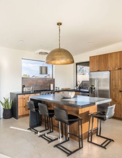 Modern kitchen interior featuring a large wooden island with black stools and brass pendant lighting.