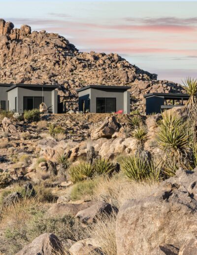 Modern houses nestled among rocky desert terrain under a sunset sky.