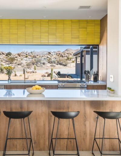 Modern kitchen interior with wooden cabinetry, a white countertop, and a desert view through large windows.