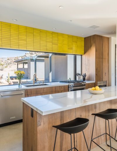 Modern kitchen interior with wooden cabinetry, stainless steel appliances, and a breakfast bar with stools.