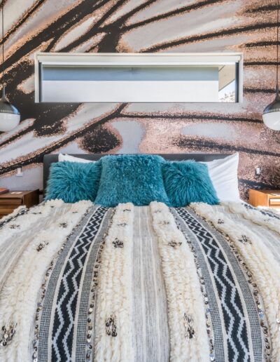 A modern bedroom featuring a large abstract wall art above the bed with plush blue and white bedding.