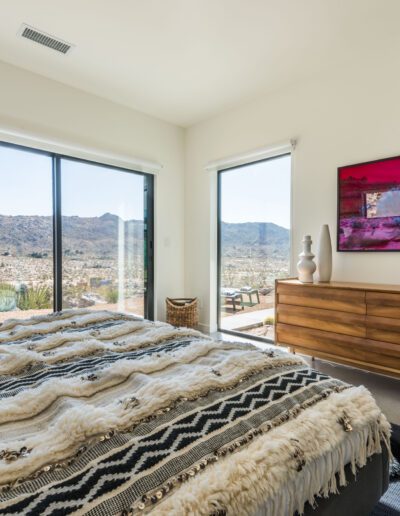 A bright and airy bedroom with a large window offering a scenic view, complemented by a modern dresser and a colorful wall-mounted television screen.