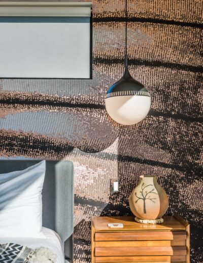 Modern bedroom detail with textured wall, hanging pendant light, wooden bedside table, and decorative vase.