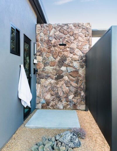 Outdoor stone-clad shower with towel hanging on the side and desert plants in the foreground.