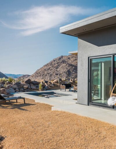 Modern desert home with outdoor seating and a hanging chair overlooking a rocky landscape.