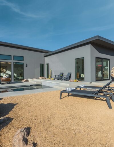 Modern single-story house with a swimming pool and patio furniture in a desert landscape.