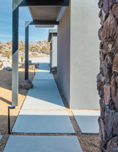 Modern desert home entrance with stone wall and geometric pathway.