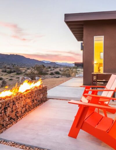 Modern patio with a fire feature and red chairs overlooking a desert landscape at dusk.