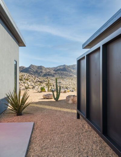 Modern desert home featuring a contrasting pink door and stone wall with mountainous background.