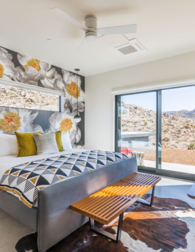 Modern bedroom with large floral wall design, overlooking a mountainous landscape through sliding glass doors.