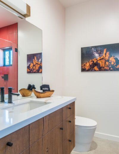 Modern bathroom interior with red tile accent wall, wooden vanity, and two framed pictures on the wall.