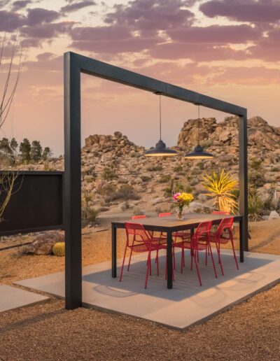 Outdoor dining area with red chairs set in a desert landscape at dusk.