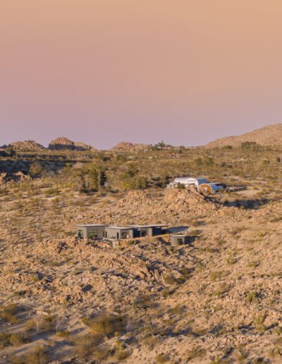 An aerial view of a modern desert home amid rocky terrain at dusk.