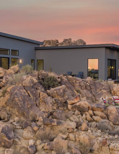 Modern desert house at twilight with rocky foreground and colorful sky.