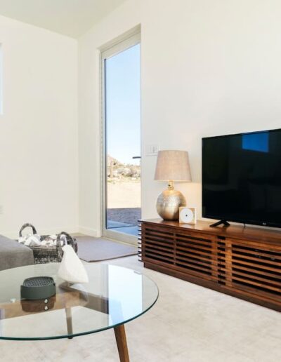 A modern living room with a grey sofa, a glass coffee table, and a television on a wooden stand.