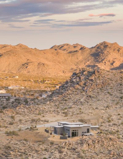 A modern home nestled in a desert landscape at sunset with rolling hills in the background.