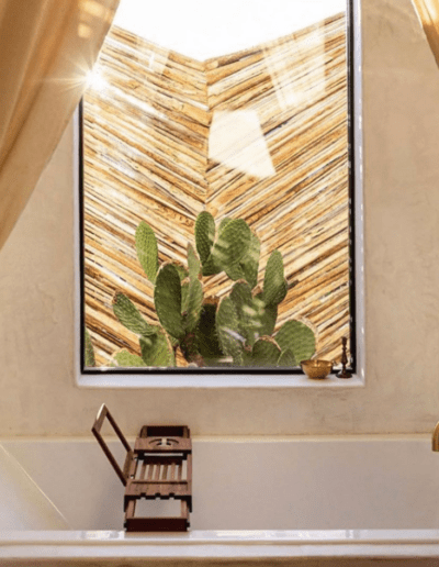 Luxurious bathroom with a large window revealing a cactus, complemented by golden fixtures and warm lighting.