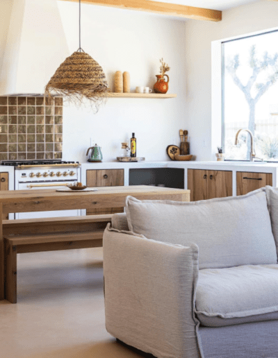 A bright, modern kitchen with wooden furniture and a beige sofa in the foreground.