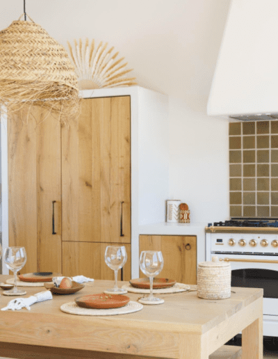 A modern kitchen with wooden furniture and neutral tones featuring a dining table set for four and a stylish pendant light above.