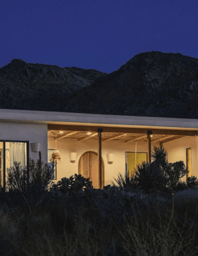 Modern house illuminated at twilight against a backdrop of rugged mountains.