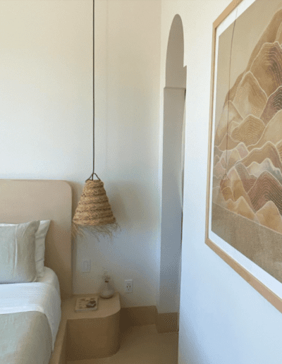 A minimalist bedroom with a hanging pendant lamp, large framed artwork, and earth-tone decor.