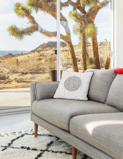 Modern living room with a gray sofa, decorative pillow, and a desert view through large windows.