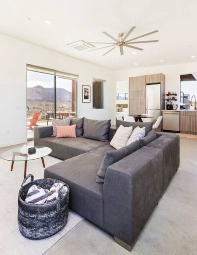 Modern living room with a large gray sectional sofa, a ceiling fan, and a mountain view through large windows.