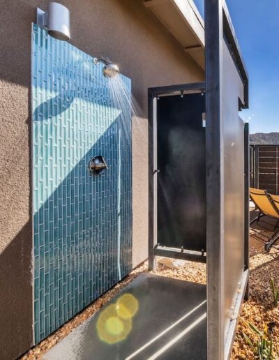 Outdoor shower with blue tile wall and open metal door.