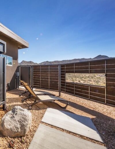 Patio area with a lounge chair facing a metal fence with a desert mountain landscape in the background.