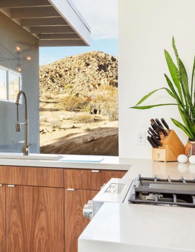 A modern kitchen with wooden cabinets and stainless steel appliances overlooking a desert landscape.