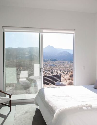 Modern bedroom with a large window offering a desert mountain view, featuring a neutral color palette and minimalist decor.