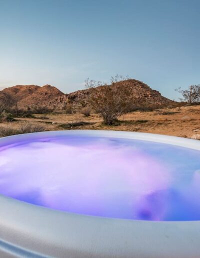 Illuminated hot tub with purple lighting set against a desert landscape at twilight.